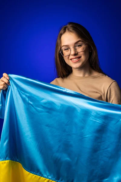 在蓝色背景下高举乌克兰国旗的年轻女子 — 图库照片