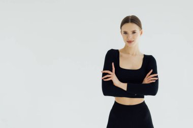 Güzel bir kız ya da fitness eğitmeni poz verip gülümsüyor, kollarını kavuşturmuş kameraya bakıyor, beyaz arka planda izole edilmiş..