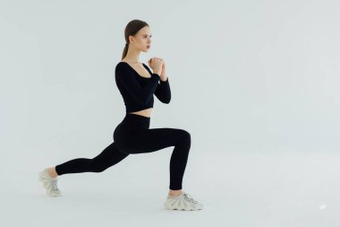 Spor salonundaki kadın esneme egzersizi yapıyor. Beyaz arka planda genç bir kadının tam boy çekimi..