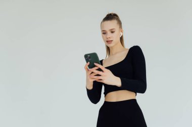 Kulaklık ve cep telefonuyla müzik dinleyen bir kadının portresi beyaz arka planda izole edilmiş.