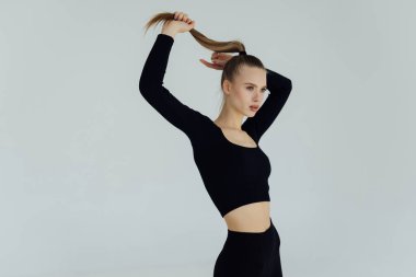 Atkuyruklu esmer, atkuyruklu kadın gri arka planda spor kıyafetleri giymekten hoşlanıyor.