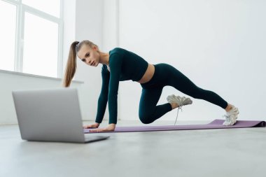 Active fit sporty young woman exercise in living room at home on mat watching online video training tutorial sport live stream workout class on laptop