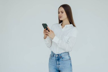 Beyaz arka planda izole edilmiş cep telefonu kullanırken gülümseyen genç esmer kadın.