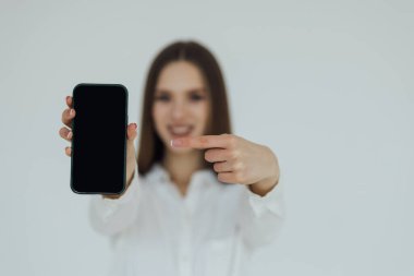 Happy young woman holding blank screen mobile phone and pointing finger over white background