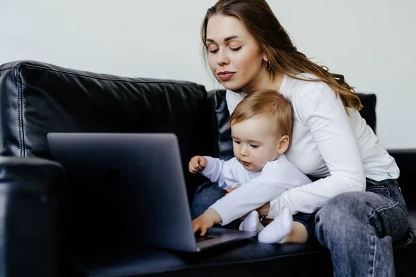 smiling freelancer pointing at laptop while holding little son