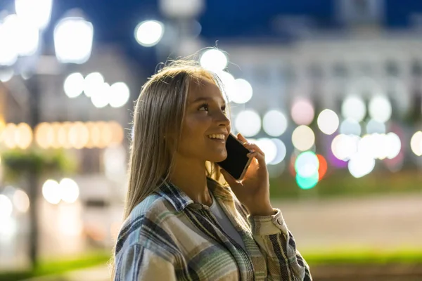 Beautiful woman talking on mobile phone, walking in night city