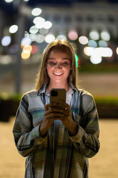 Night portrait of blonde girl using mobile phone on street
