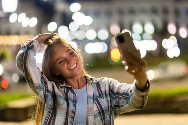 Beautiful woman makes selfie on the phone in the night city.