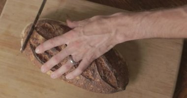 Adam kesme tahtasına taze bir somun zanaatkar ekmeği kesiyor..