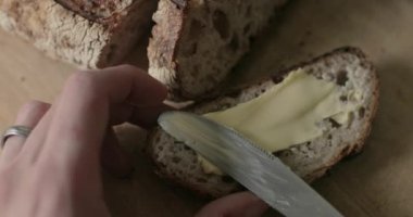 İnsan taze dilimlenmiş bir parça ekmeğe tereyağı sürer..