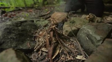 Ateş çemberindeki dalları kullanarak kamp ateşi yakan bir adamın el kamerası görüntüsü..