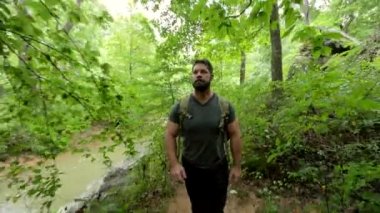 Sırt çantasıyla gezen bir adam, akan bir nehrin yanındaki sık bir ormanın içinden geçiyor..