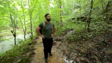 Sırt çantasıyla gezen bir adam, akan bir nehrin yanındaki sık bir ormanın içinden geçiyor..