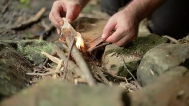 Ateş çemberindeki dalları kullanarak kamp ateşi yakan bir adamın el kamerası görüntüsü..