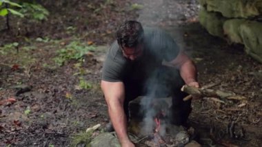 Erkek bir kampçı, yanan bir kamp ateşinde odun topluyor. Yavaş çekimde, yüzeysel bir odak ile..