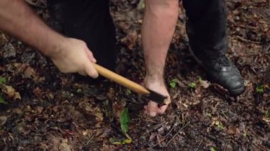 Erkek bir kampçı, hayatta kalma sığınağı olarak, yavaş çekimde bir çadır kazığını yere çakar..