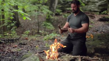 Erkek bir kampçı, yavaş çekimde yanan bir kamp ateşine sığ bir odak ile yapışır..