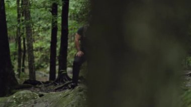 Erkek bir yürüyüşçü, bir ayağı kayanın üzerinde ağır çekimde yolculuğundan sonra dinleniyor..