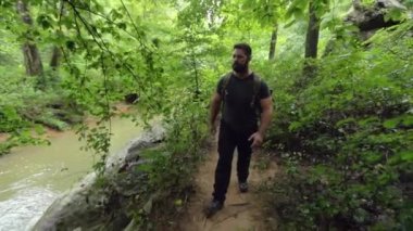 Bir erkek yürüyüşçü yol boyunca bir nehrin kenarında ağır çekimde yürür..