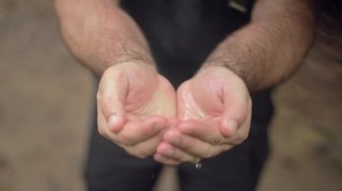 Erkek bir yürüyüşçü ellerini yağmurda yıkar. Yavaş çekimde damlar..