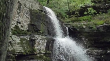 Yavaş çekimde akan bir şelaleyle aşağı doğru, büyük bir uçurum yüzeyi ve kayanın yanına..