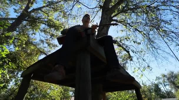 Teenagerjunge Spielt Gitarre Auf Einer Baumplattform Silhouette Zeitlupe Gegenlicht Der — Stockvideo