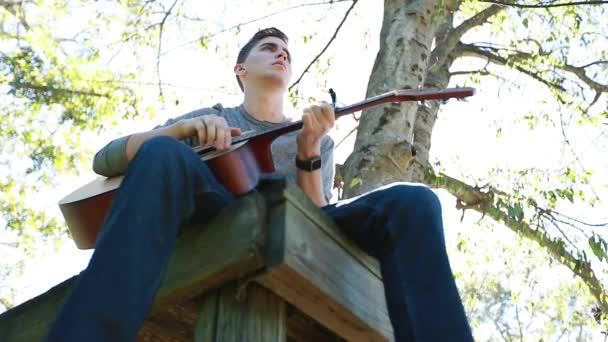 Мальчик Подросток Играет Гитаре Дереве Медленное Движение Подсвечено Ярким Послеобеденным — стоковое видео