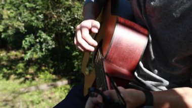 Genç bir çocuk, ağaç platformunda gitar çalarken detay, parlak öğleden sonra güneşiyle yavaş çekim arka planda..