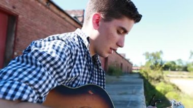 Genç çocuk arka planda eski bir tuğla bina ile yavaş çekimde gitar çalar..