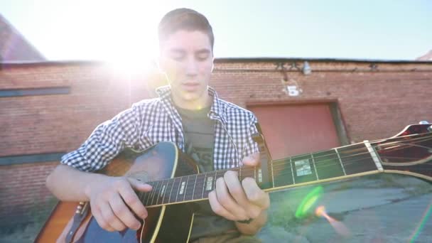 Teenage Boy Hraje Kytaru Zpomaleném Filmu Starou Cihlovou Budovou Pozadí — Stock video