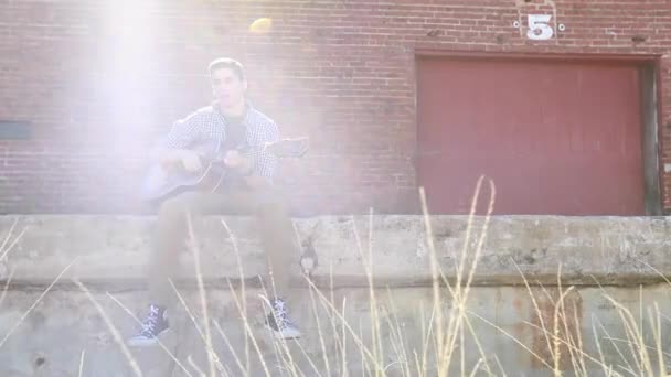 ティーン男の子演劇ギターでスローモーション近く草とともに古いですレンガ造りの建物で背景 — ストック動画