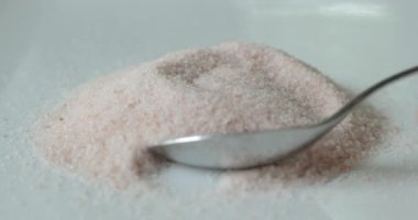 Beyaz bir tabakta pembe Himalaya tuzu ve kaşıkla kepçelenmiş..