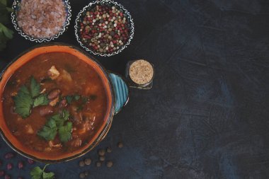 Kırmızı fasulye çorbası, otlar ve baharatlar koyu masa arkasında. Kopyalama alanı olan üst görünüm.