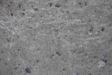 Rough gray dry concrete wall surface interspersed with fine black crushed pebbles and light stripes close-up industrial texture for the background