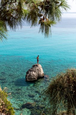 Lefkada adası. Yunanistan - 08.05.2021: Güzel turkuaz denizine dalmaya hazır bir kayanın üzerinde duran turist.