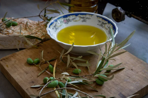 Yeşil zeytin ve dal bir kase ve bir şişe soğuk zeytinyağı ile ahşap bir tahtanın üzerinde.