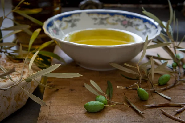 Yeşil zeytin ve dal bir kase ve bir şişe soğuk zeytinyağı ile ahşap bir tahtanın üzerinde.