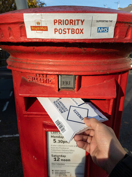 London.UK- 11.05.2021. A Royal Mail Priority Post Box with a person posting a Covid-19 test package.