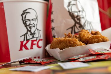 Londra mı? UK- 06.06.2020: KFC 'den (Kentucky Fried Chicken) tavuk filetoları, üzerinde şirket logosu ve imzası bulunan bir kova ve bir masa üstü ketçap ve mendil paketleri ile birlikte..