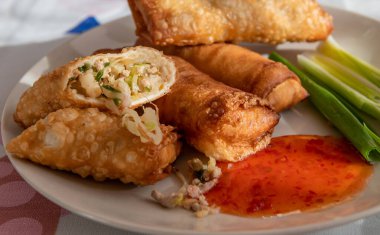 Bir tabak bütün ve çıtır çıtır börek sebze ve et dolgularını, sosu ve taze soğanları gösteriyor..