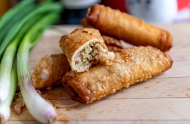 Yarısı doğranmış ve taze soğan servis etmeye hazır ahşap bir tahtanın üzerinde çıtır çıtır börekler..