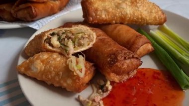 Bir tabak bütün ve çıtır çıtır börek sebze ve et dolgularını, sosu ve taze soğanları gösteriyor..