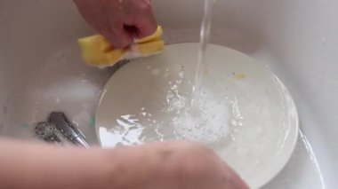 Mutfak lavabosunda kirli tabağı yıkayan bir insanın yavaş çekimde akan suyun altında.