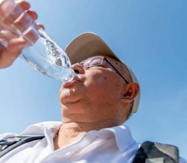 A senior man drinking plenty of water on a record breaking hot summer day to avoid dehydration while out and about.