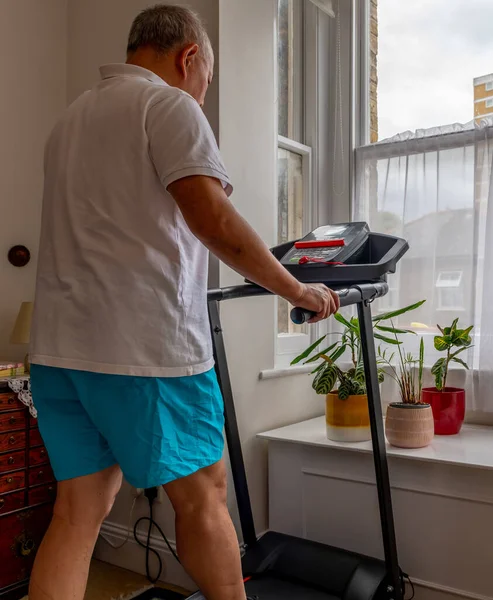 A senior man trying to keep fit working out on a treadmill at home.