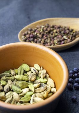 Kil kapta kardamon, tahta kaşıkta sichuan kağıdı ve koyu gri kumaş üzerinde ardıç meyvesi.