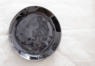 Açık kumaş bir masada siyah bir tabak..