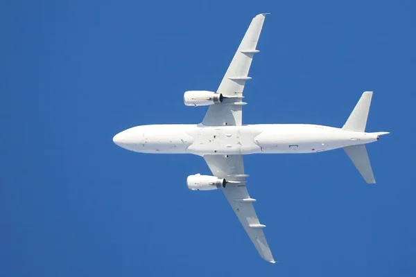 A white plane in flight on a blue sky background, bottom view — Stock Photo, Image