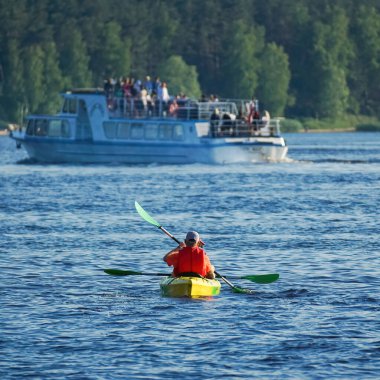 Kırmızı yelekli iki kişi, mavi sularda bir kano üzerinde kürek çekiyorlar.