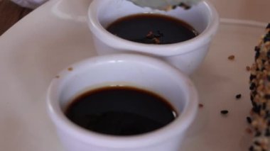 Kaliforniya Maki 'sini ahşap yemek çubuklarıyla 4K' deki bir lokantada beyaz bir tabakta sosa batırmak.
